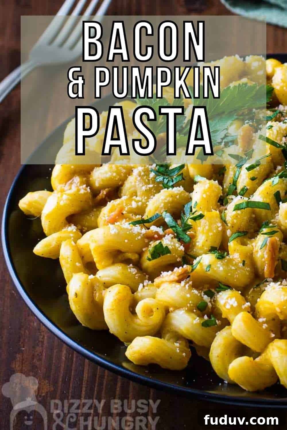 Side close up shot of pumpkin pasta garnished with herbs on a black plate with a fork and tablecloth in the background on a wooden surface.