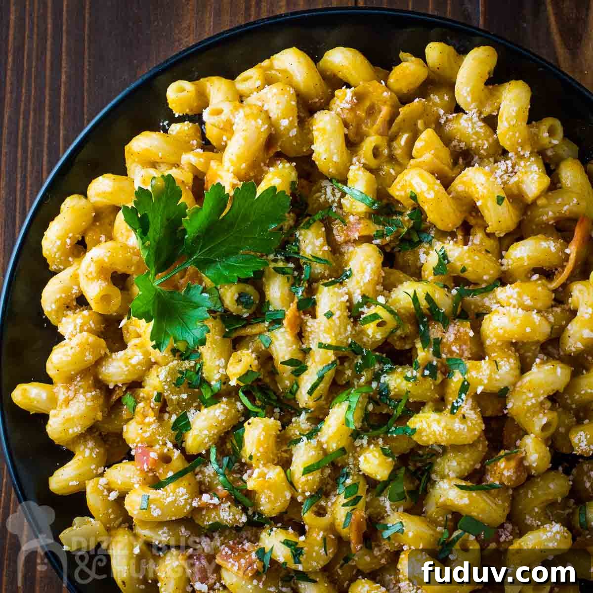 Overhead close up shot of pumpkin pasta garnished with herbs on a black plate on a dark wooden surface.