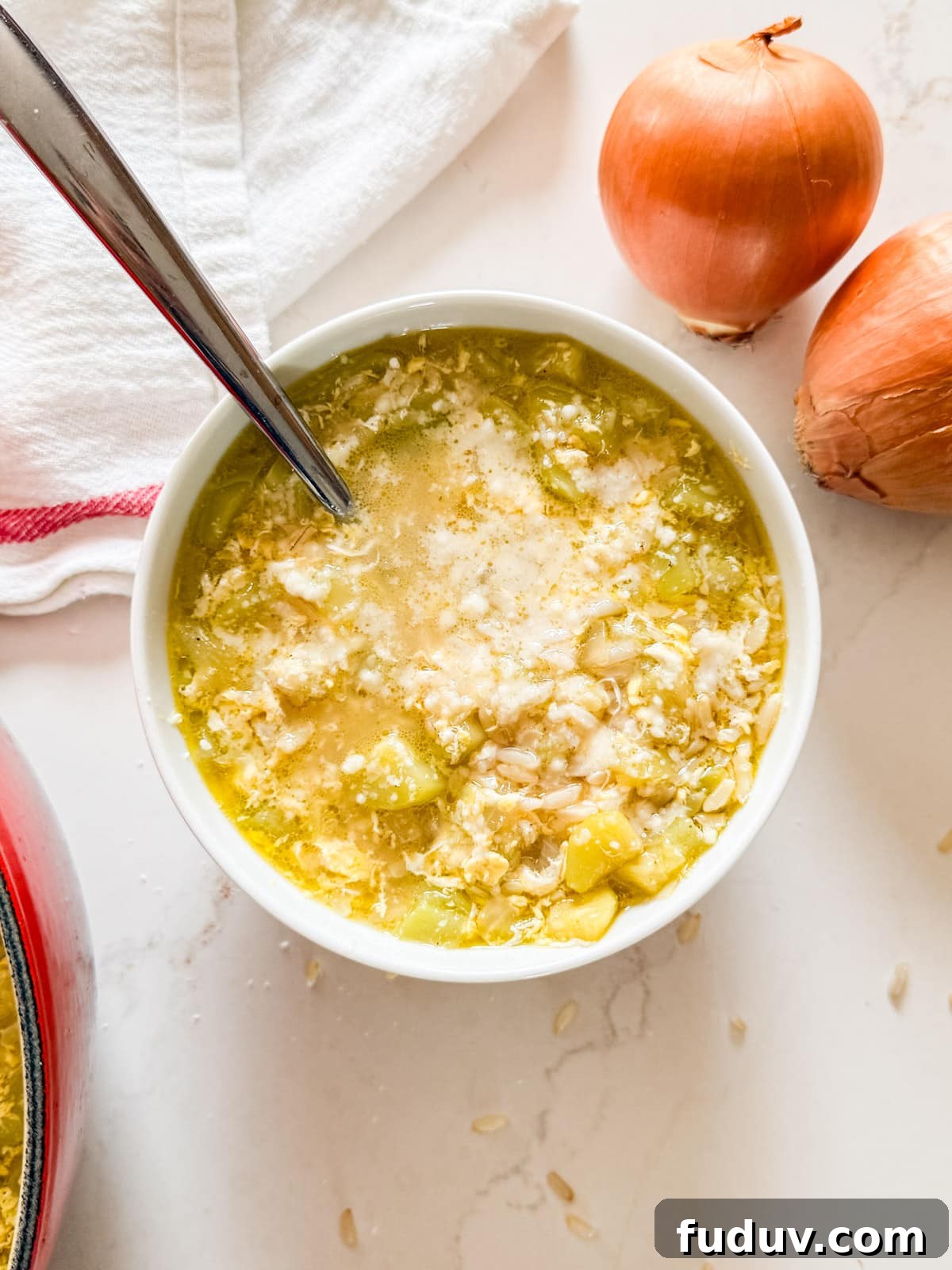 An overhead image of a bowl of zucchini soup with onions and a tea towel next to it.