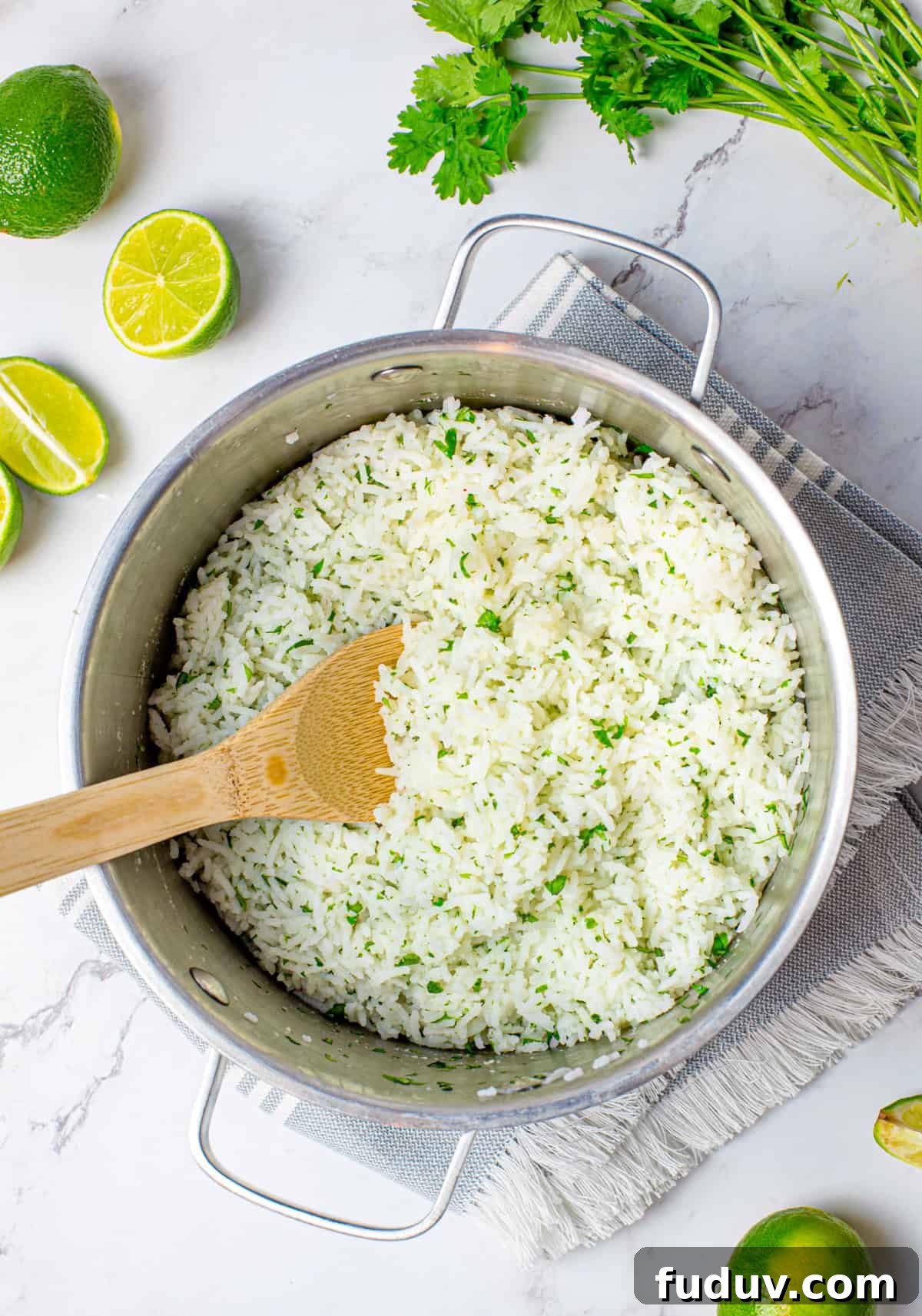 Cilantro Lime Rice Recipe: Flavorful Side Dish in 20 Minutes 3 Finished lime rice in pan with wooden spoon surrounded by limes and cilantro