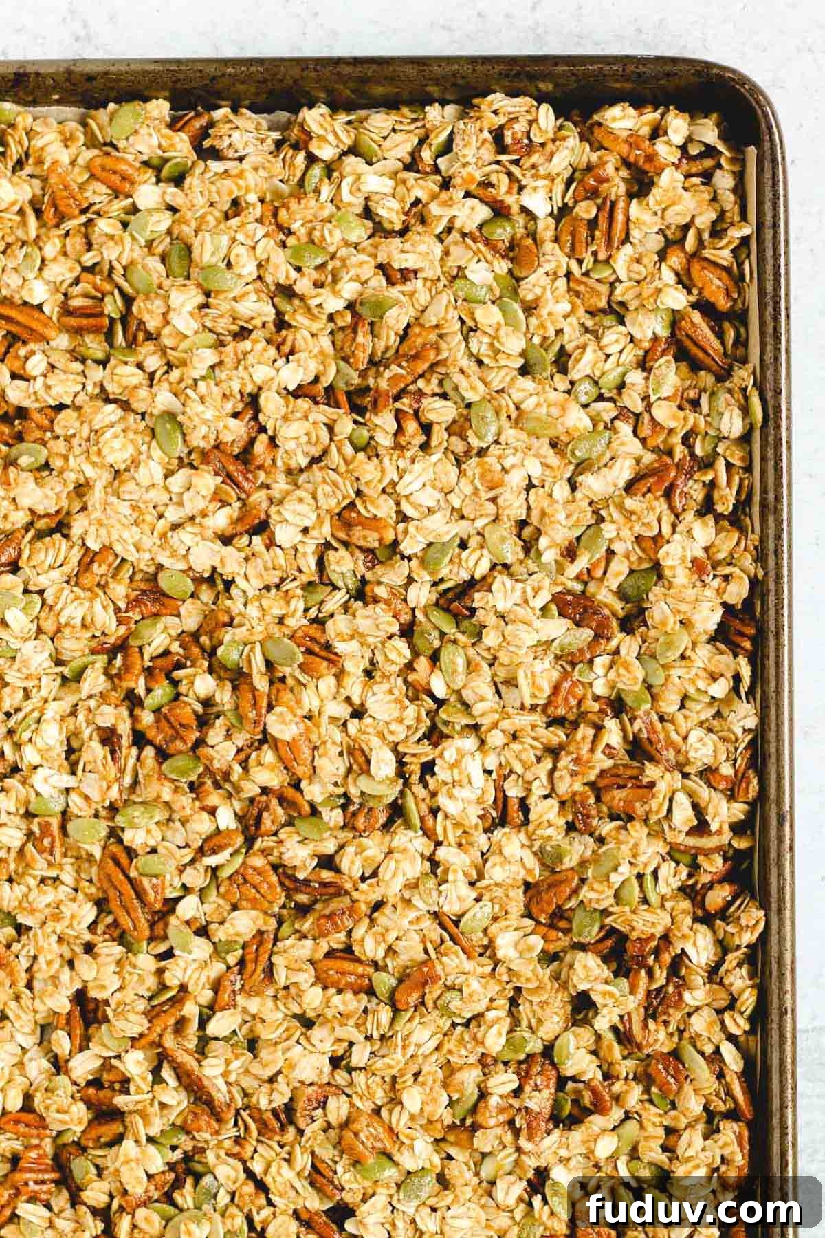 Pumpkin granola spread out no baking sheet before baking.