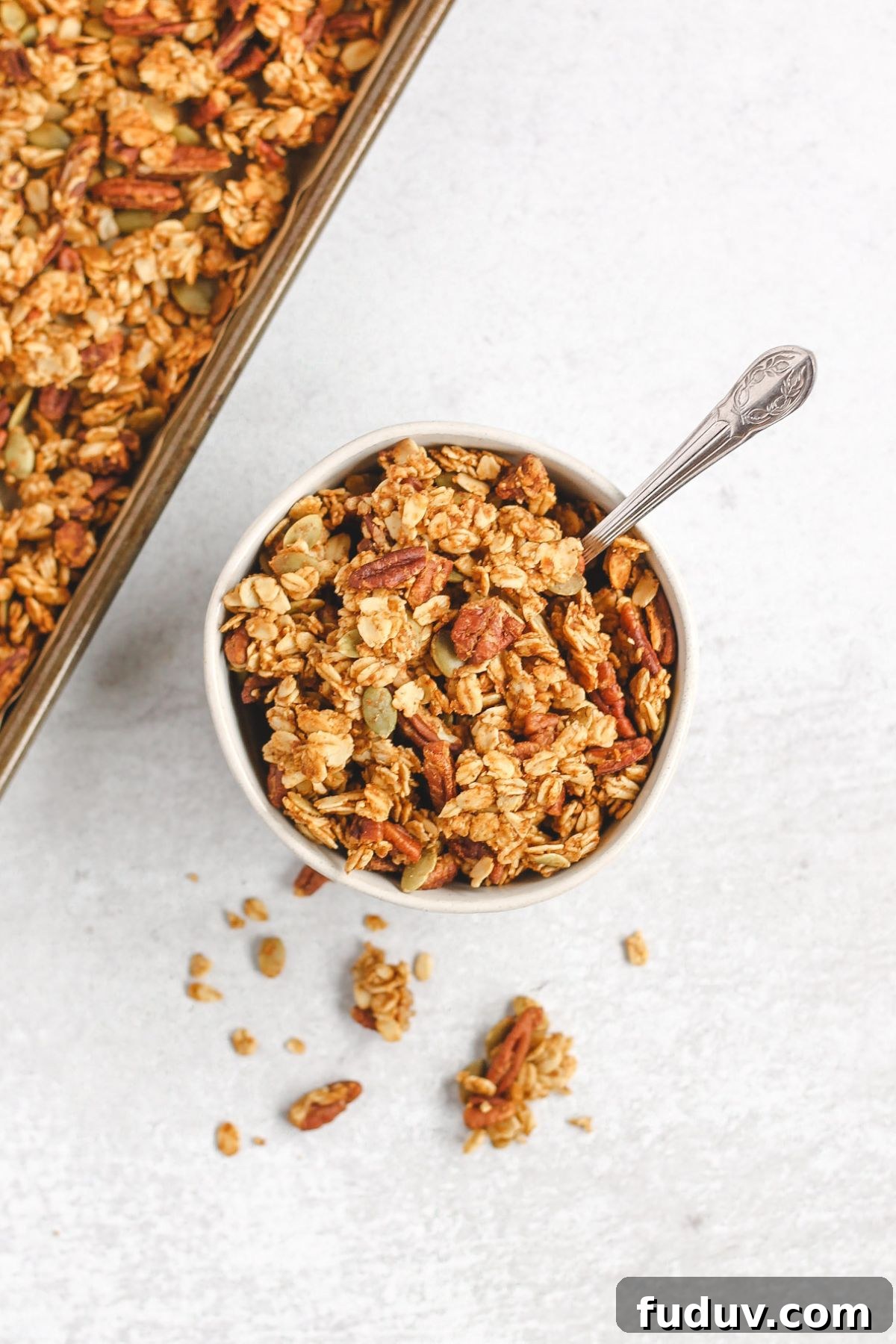 Pumpkin granola in a small bowl with a vintage spoon sitting next to baking sheet with granola.