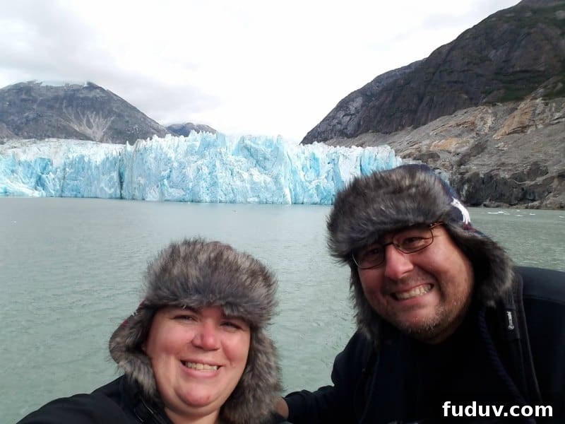 Tammilee and John smiling on a boat in front of a glacier in Alaska 