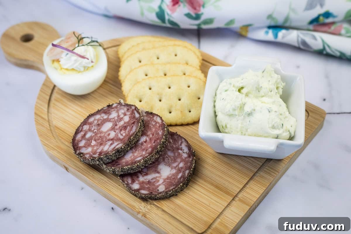 A wooden board with sliced salami, crackers, a deviled egg, and a square dish of homemade Boursin cheese.