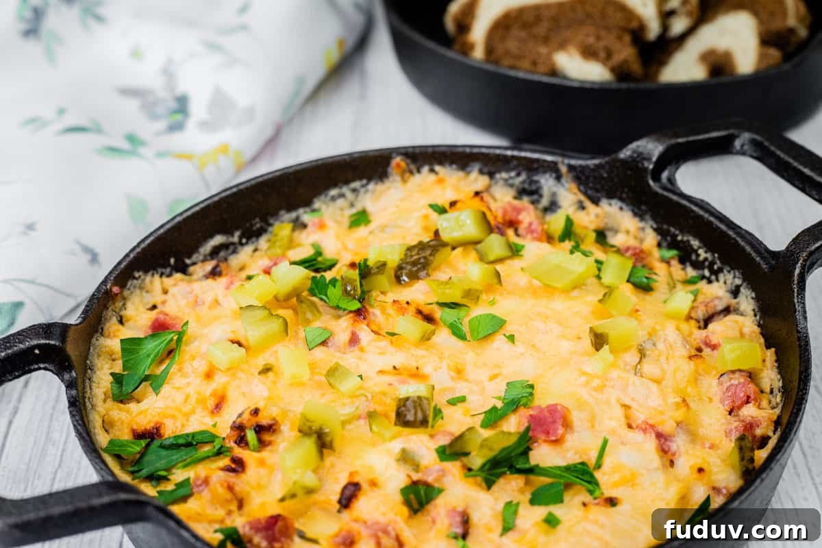 Cheesy, golden-brown Hot Reuben dip in a cast-iron skillet, topped with chopped pickles and fresh parsley, served with slices of marbled rye bread.