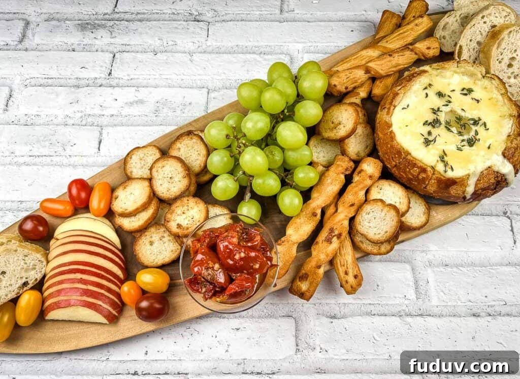A wooden platter with baked brie in a bowl, cheese, crackers, grapes and bread.