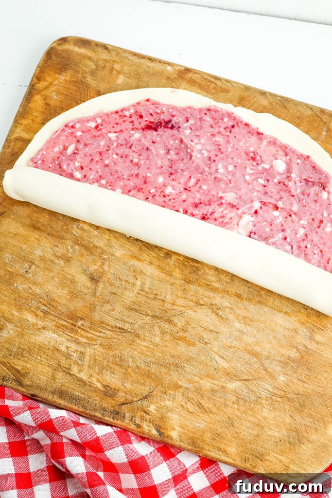 Rolling pie dough with Raspberry cream cheese filling on wooden cutting board.