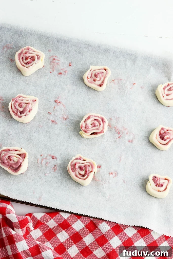 Sliced Raspberry pinwheels on cookie sheet lined with parchment paper.