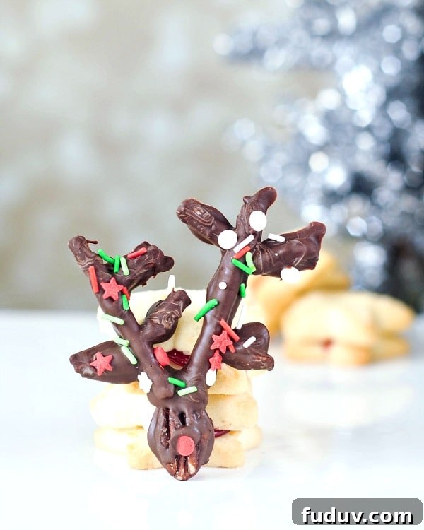 a chocolate covered pecan and pretzel reindeer propped up against a stack of shortbread cookies, silver holiday tree in background