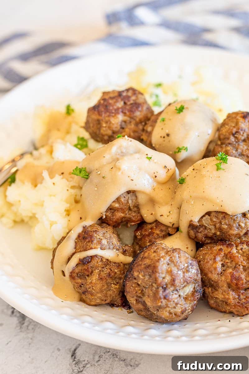 Swedish meatballs served on a white plate with mashed potatoes and gravy.