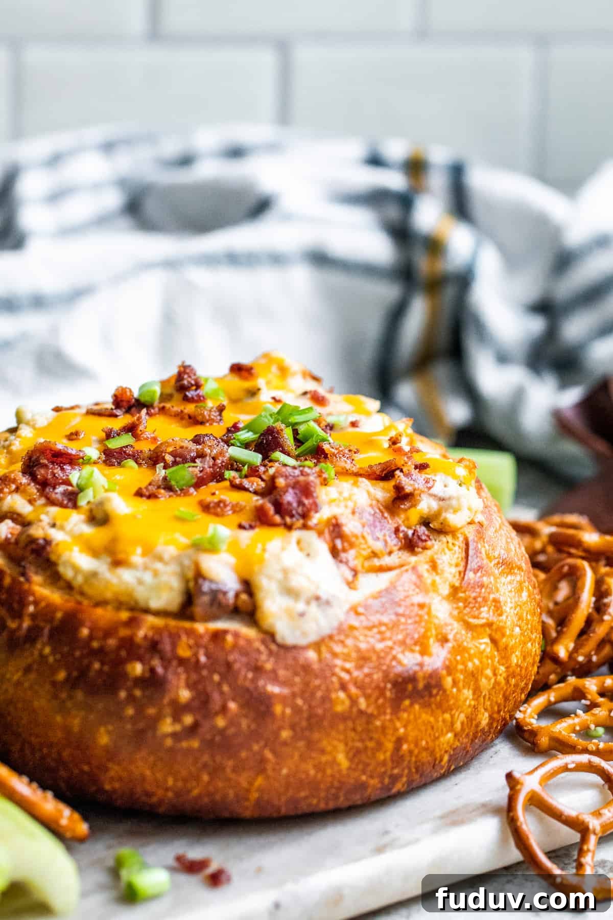 Bacon cheese dip in a bread bowl with dippers on a white counter.