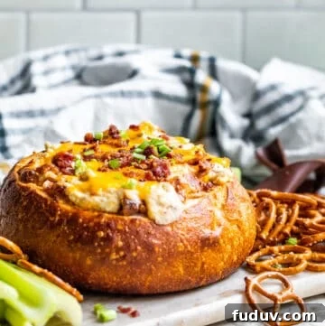 Baked dip in a bread bowl on white counter sitting on serving tray.