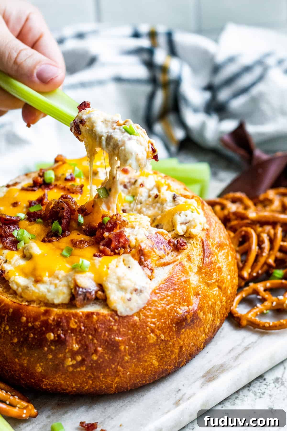 Celery being dipped into bacon dip in bread bowl.