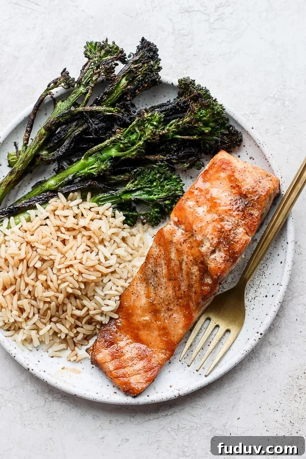 A plate with a grilled salmon filet, grilled broccolini and brown rice. 