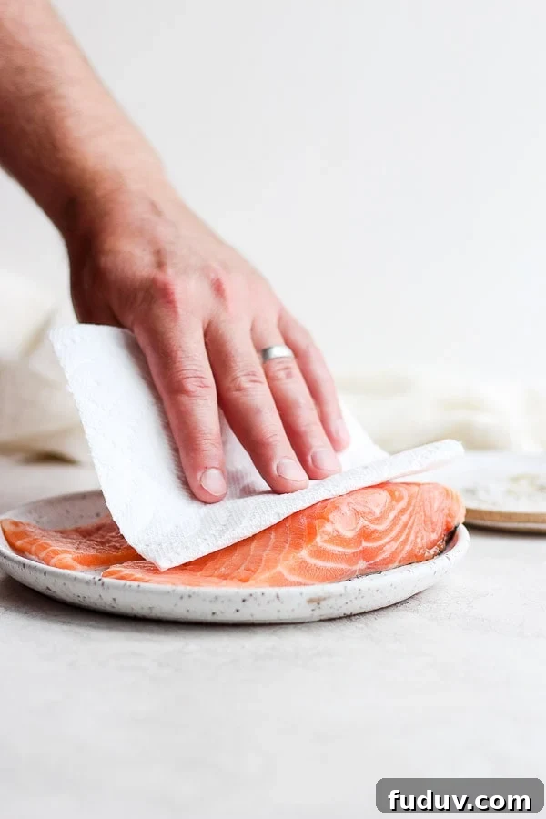 Someone patting dry a piece of raw salmon with a paper towel as they prep it for the grill. 