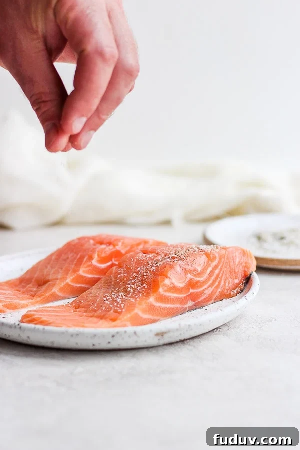 Someone sprinkling salmon filets with salt and pepper. 