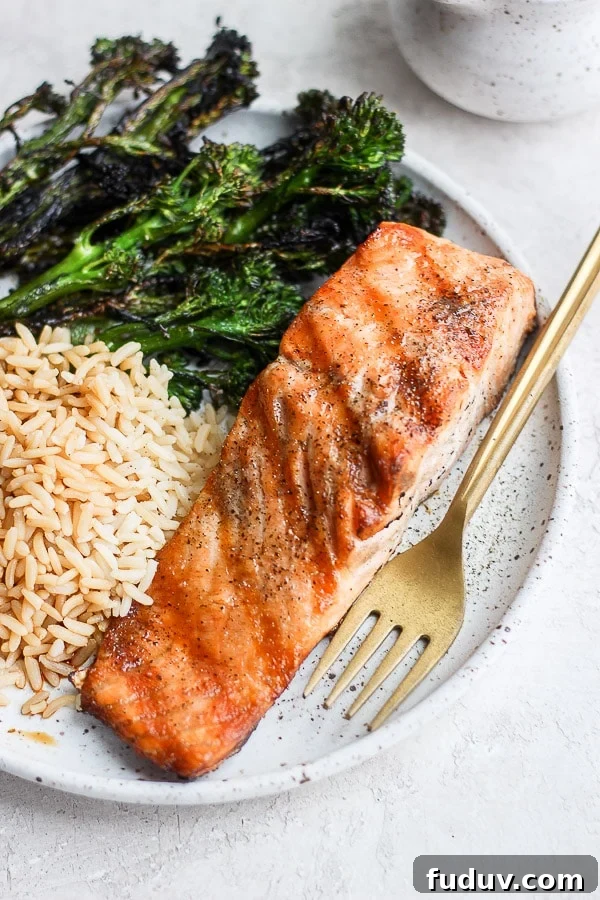 A plate with a grilled salmon filet, grilled broccolini and brown rice. 