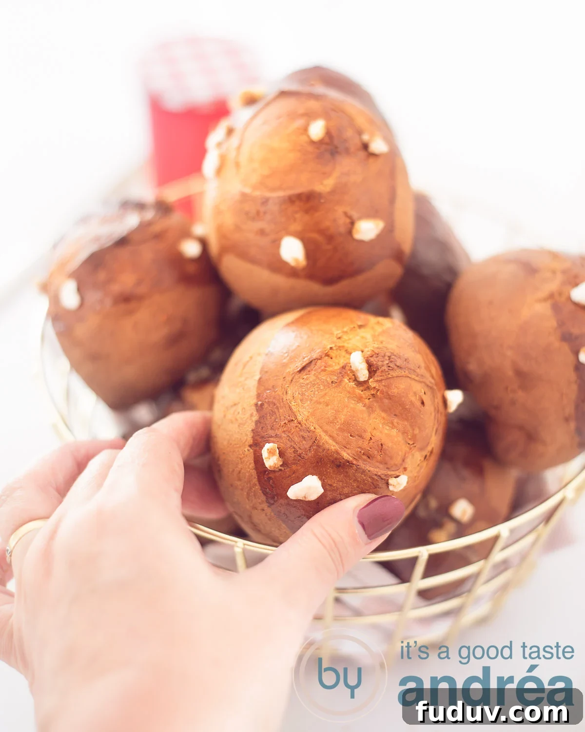 Dutch Suikerbrood: Traditional Cinnamon Sugar Buns Recipe 5 A golden wire basket filled with sugar buns on a white background. A hand grabs a bun.