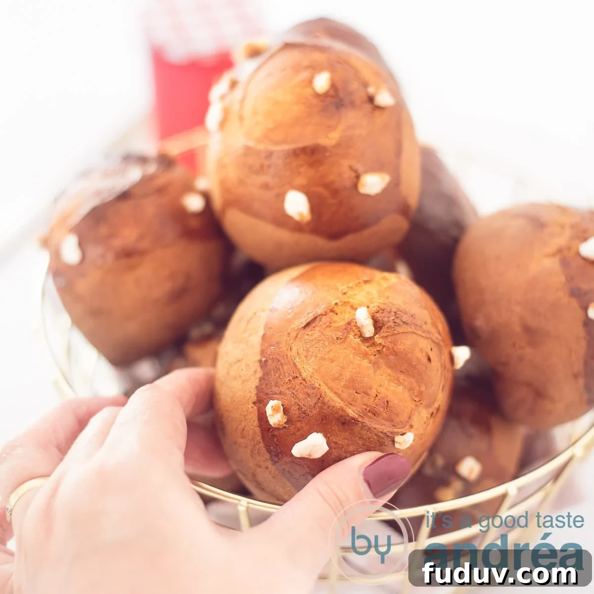 Dutch Suikerbrood: Traditional Cinnamon Sugar Buns Recipe 6 A square photo with a basket full of sugar balls with pearl sugar on a white background. A hand grabs a sandwich