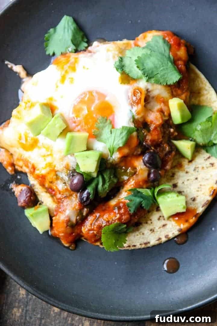 Baked Huevos Rancheros Recipe: Flavorful Rancher’s Eggs Casserole 6 Fried Eggs and sauce on a tortilla on a black plate.