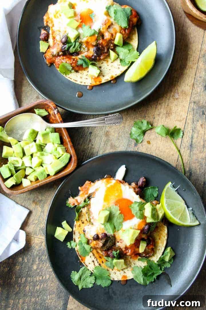 Baked Huevos Rancheros Recipe: Flavorful Rancher’s Eggs Casserole 7 Two plates of huevos ranceheros served on corn tortillas on black plates.