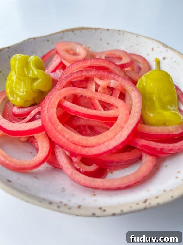 A plate with thinly sliced pickled red onions and two yellow pepperoncini peppers on a speckled white dish.