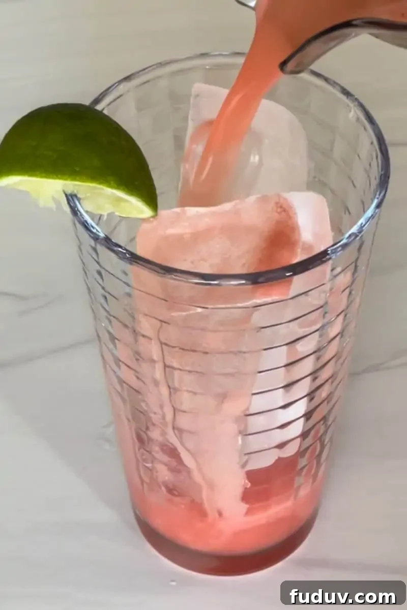 Watermelon Water being poured into a glass of ice with a lime wedge. 