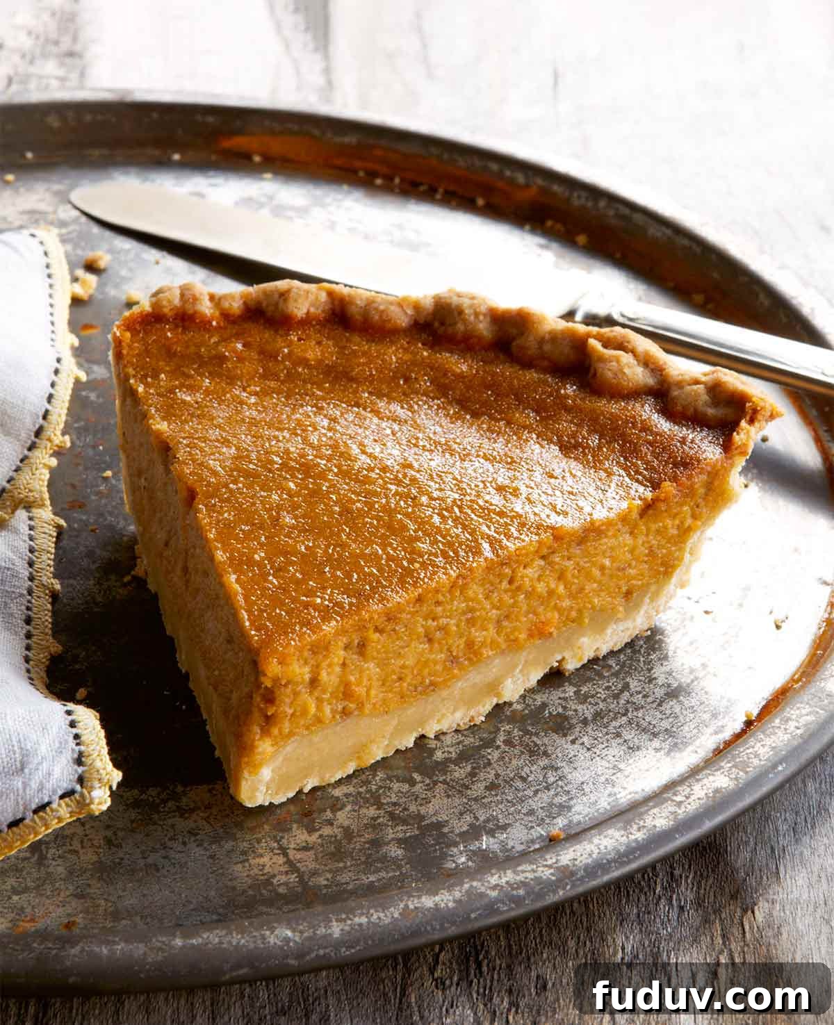 A slice of sweet potato pie on a large metal plate with a napkin and a knife.