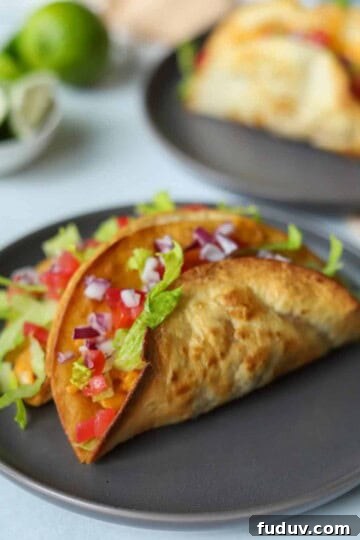 two chicken tacos topped with lettuce, onion and tomato on gray plate