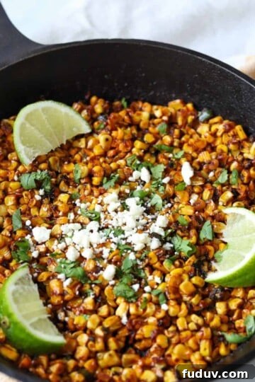 cast iron skillet filled with charred blackened corn topped with feta, cilantro and lime wedges