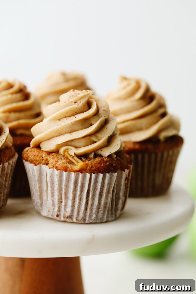 Apple pie cupcakes are a twist on a classic dessert. They are moist, delicious and with fresh apple pie filling in the middle, they give you JUST the right amount of texture! Close up of an apple pie cupcake on a cake stand.