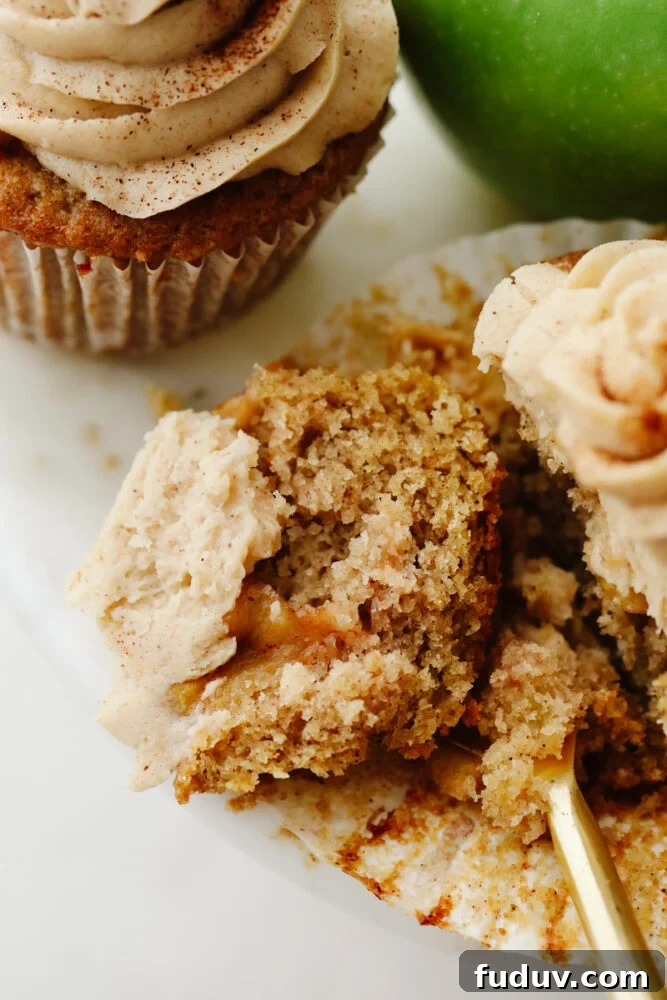 Apple pie cupcakes are a twist on a classic dessert. They are moist, delicious and with fresh apple pie filling in the middle, they give you JUST the right amount of texture! An apple pie cupcake being cut into with a fork.
