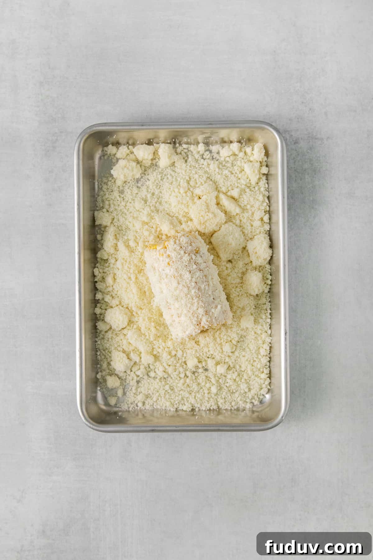 Corn on the cob being rolled in cotija cheese.