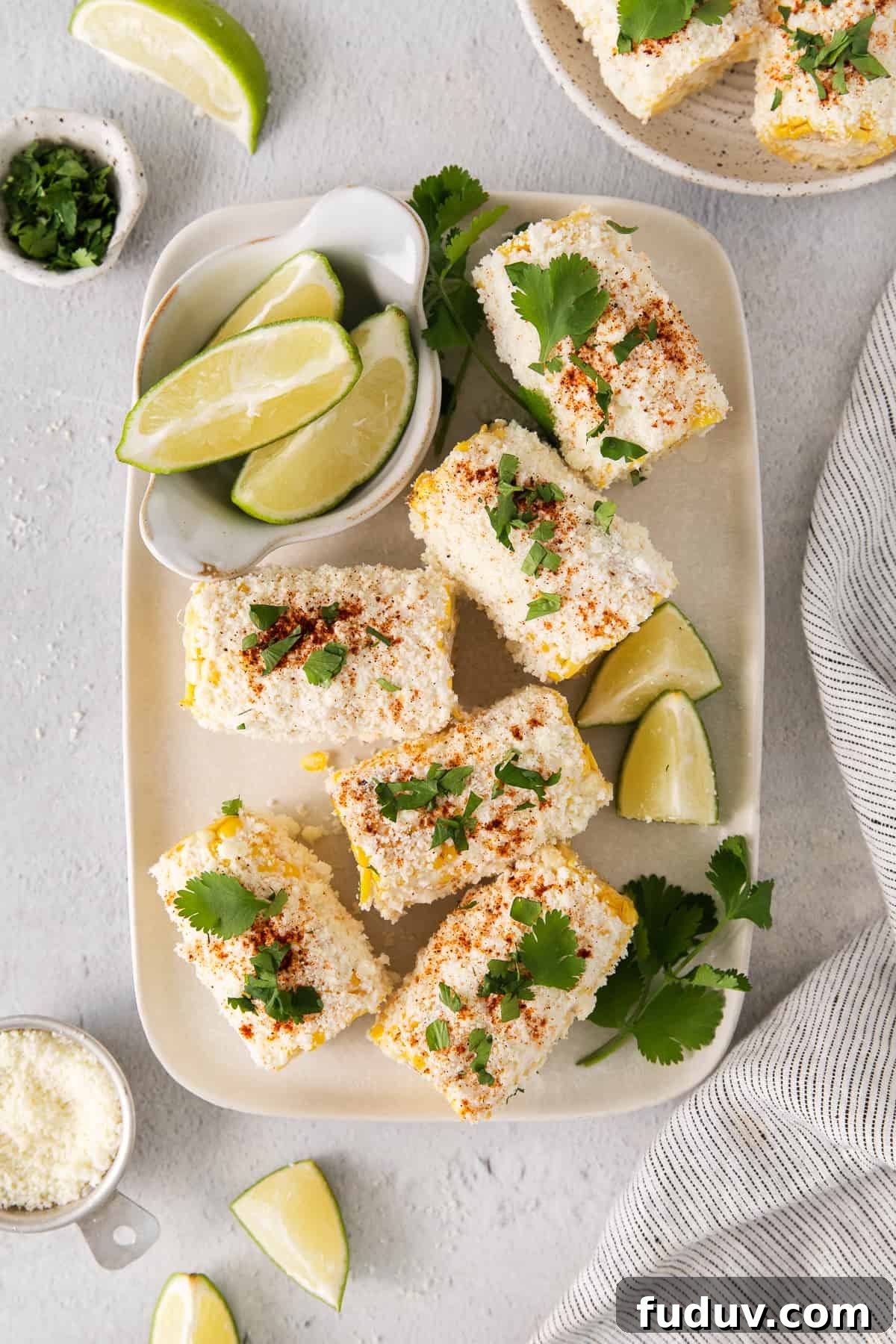 Elote corn on a plate with slices of lime.