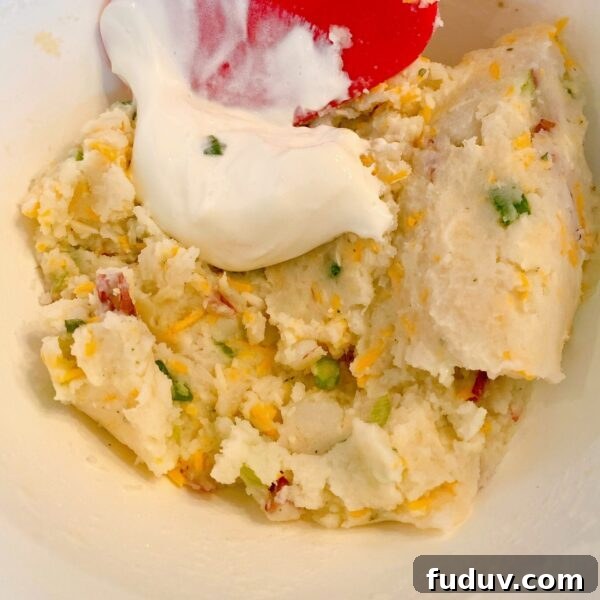 Adding sour cream to mashed potato mixture.