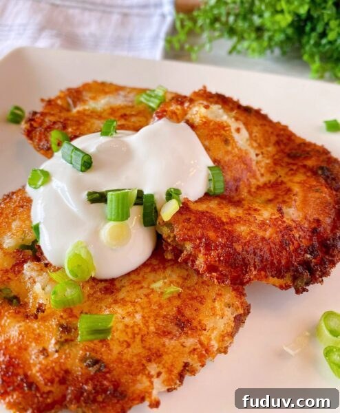 Three Loaded Mashed Potato Cakes on a plate with sour cream and chopped onions