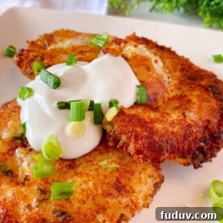Three Loaded Mashed Potato Cakes on a plate with sour cream and chopped onions