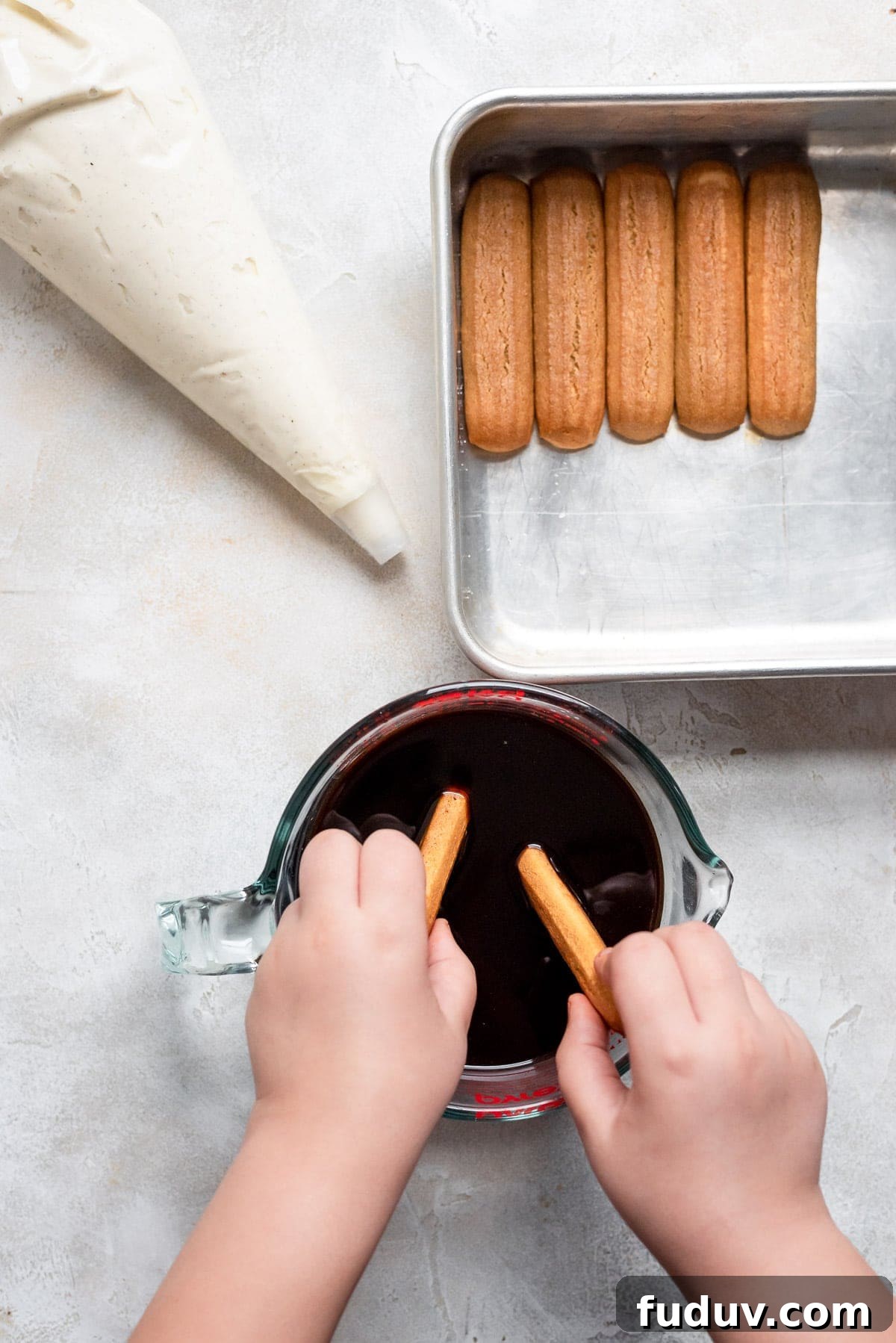 hands dipping ladyfingers in coffee and liqueur
