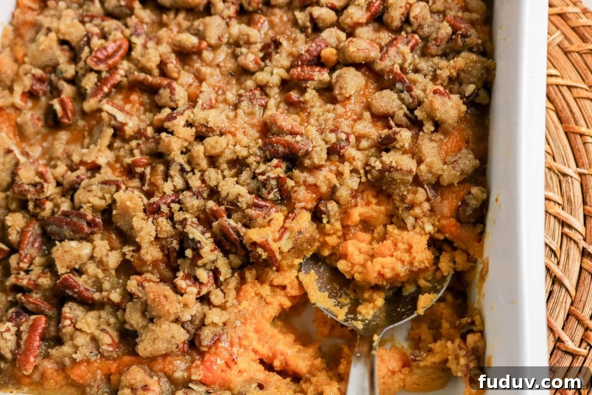 Sweet Potato Casserole Made with Canned Yams — Quick Holiday Side 11 Top down view of a serving spoon scooping a portion of sweet potato casserole with pecan topping from a white baking dish - Hostess At Heart