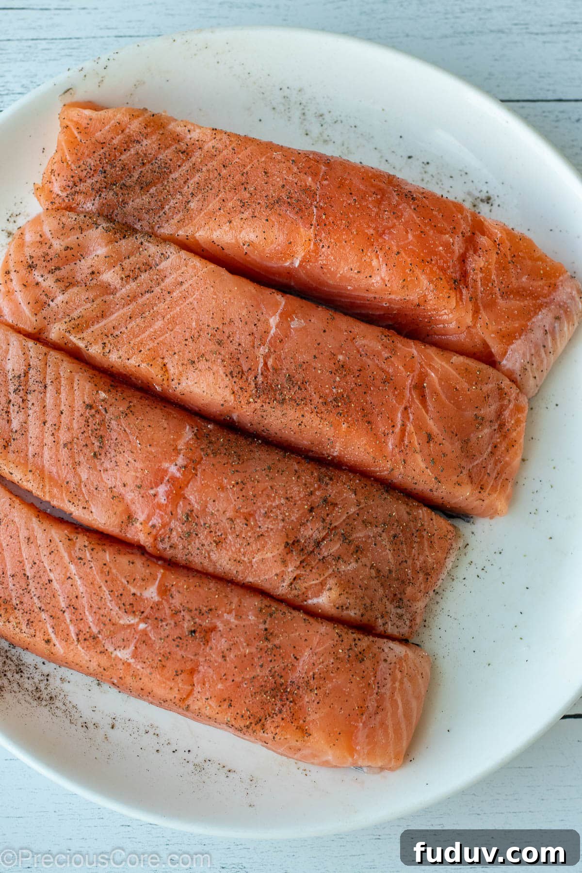 4 salmon fillet on a white plate, seasoned with salt and pepper.
