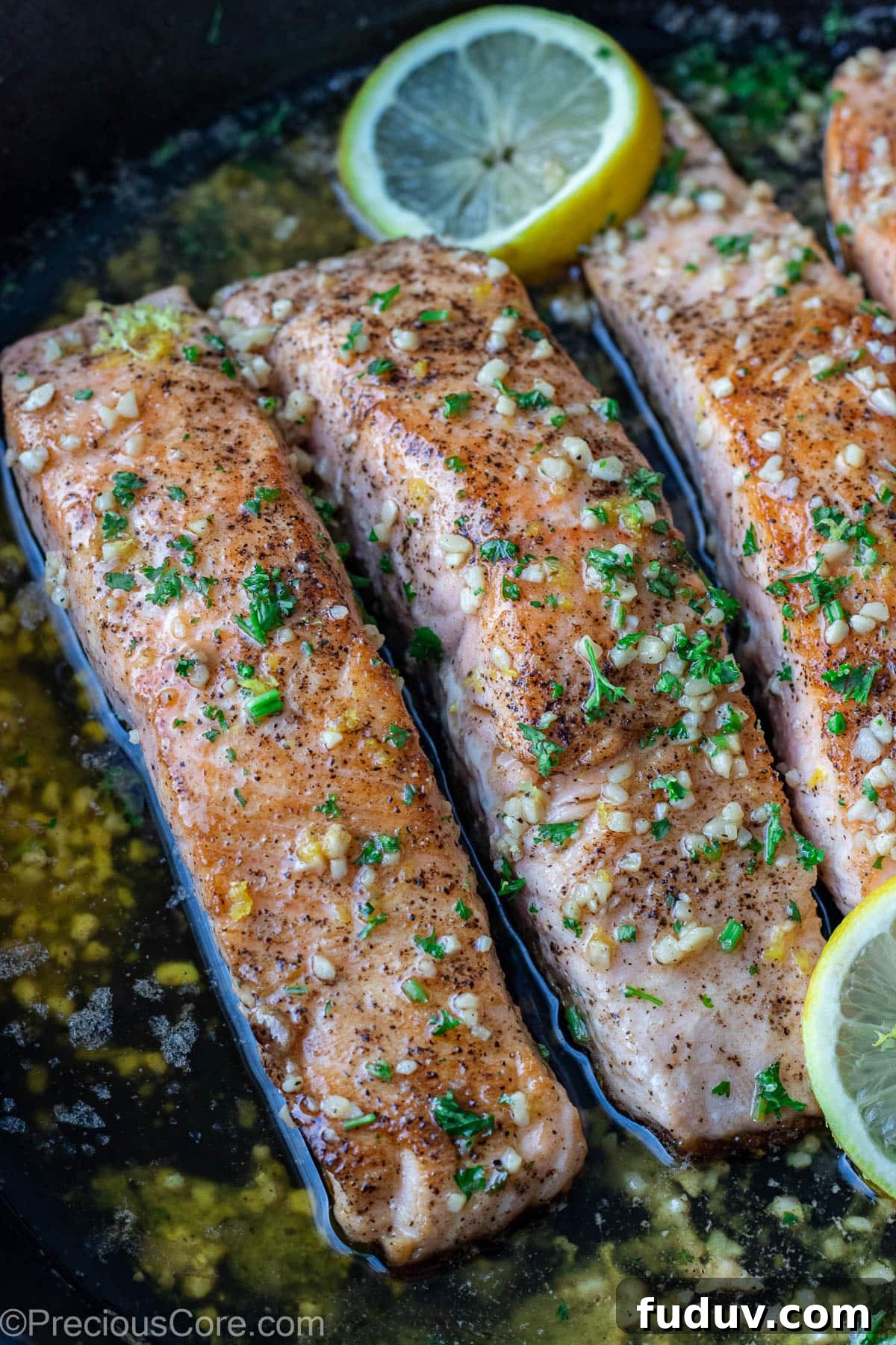 Lemon butter salmon in pan garnished with parsley and lemon slices.