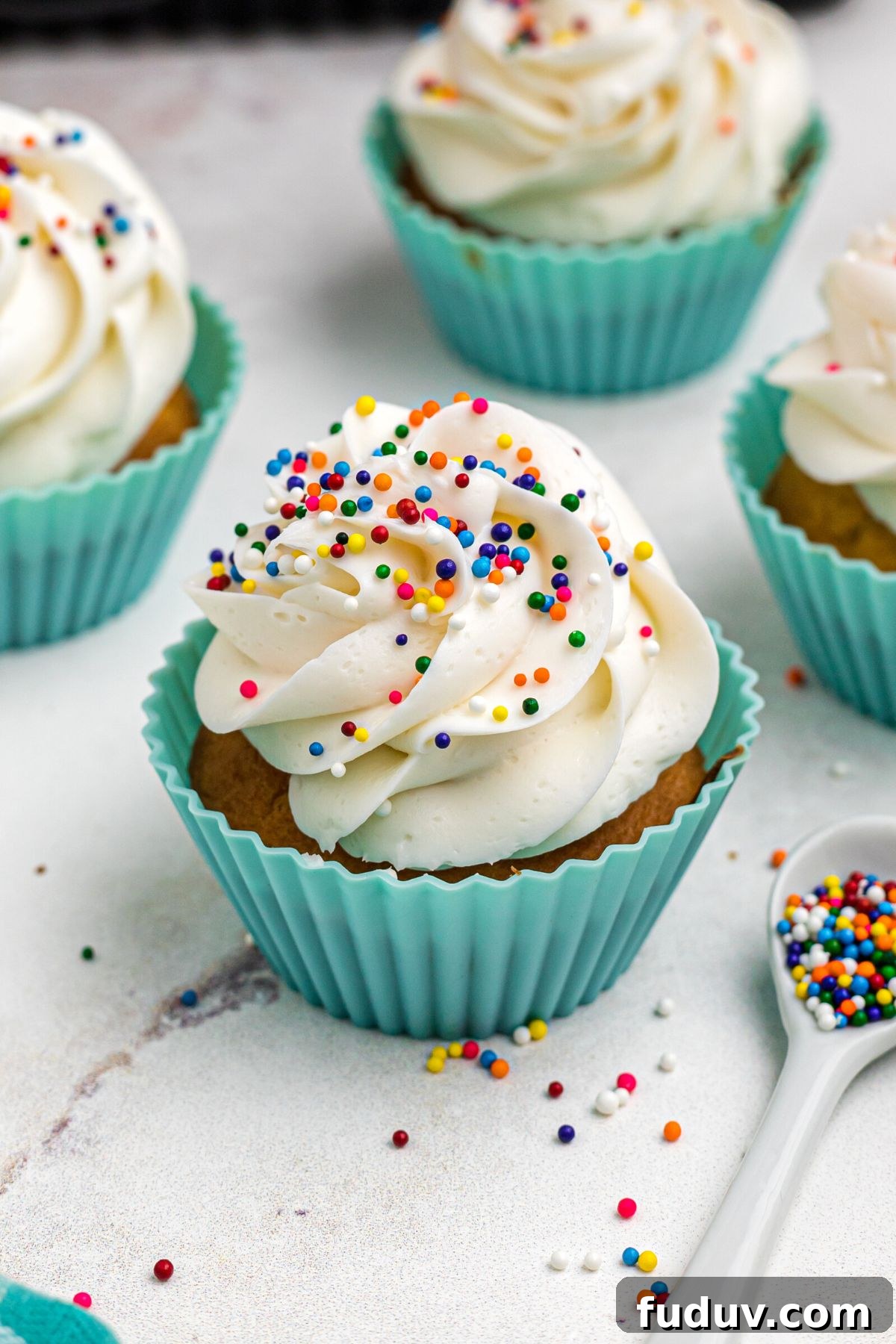 Air fryer cupcakes topped with frosting and sprinkles on a marble table.