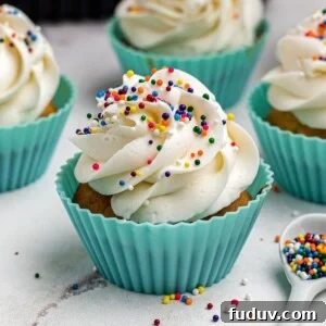 Air fryer cupcakes frosted and topped with sprinkles in front of the air fryer.