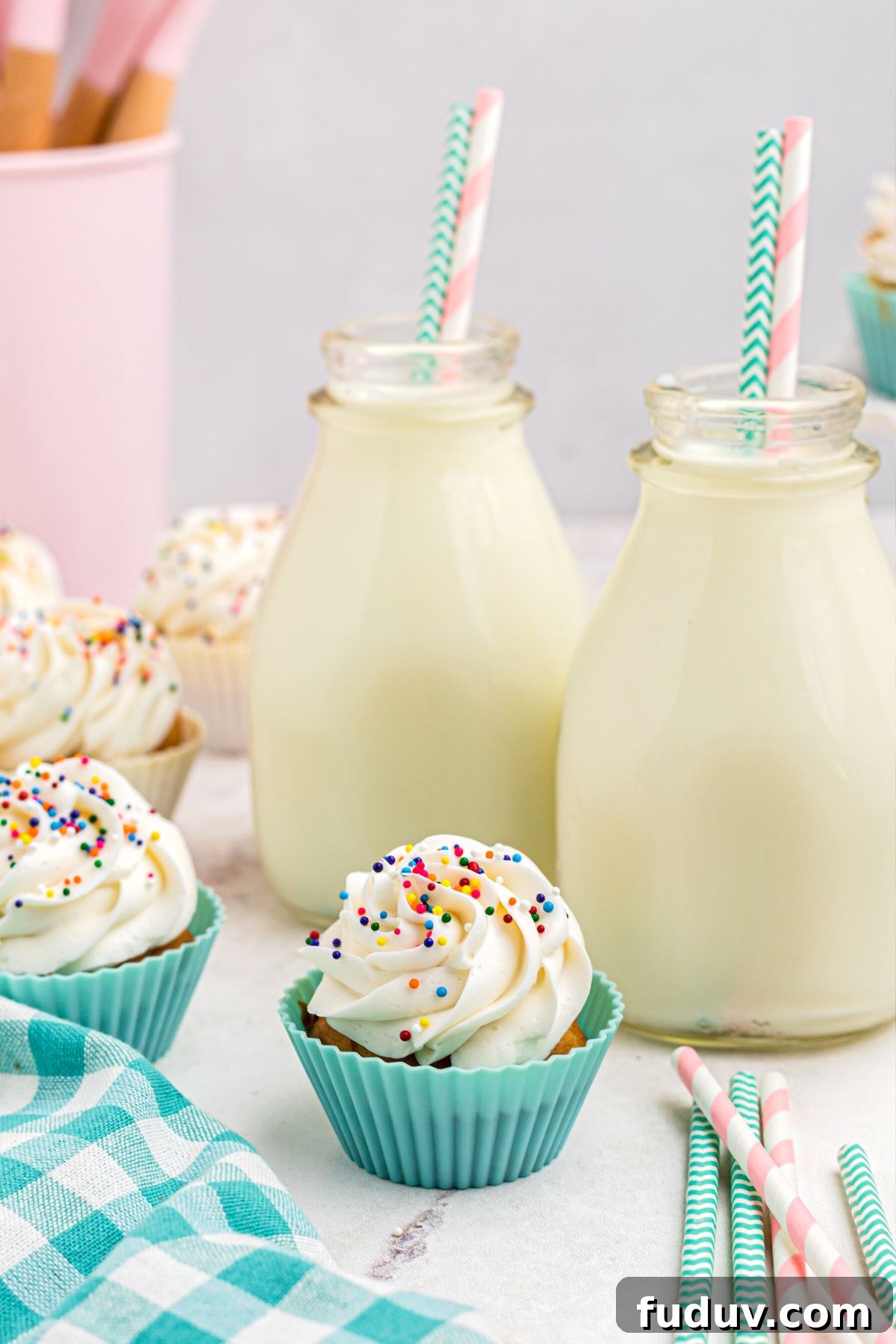 Frosted air fryer cupcakes in front of two bottles of milk with straws on a marble table.