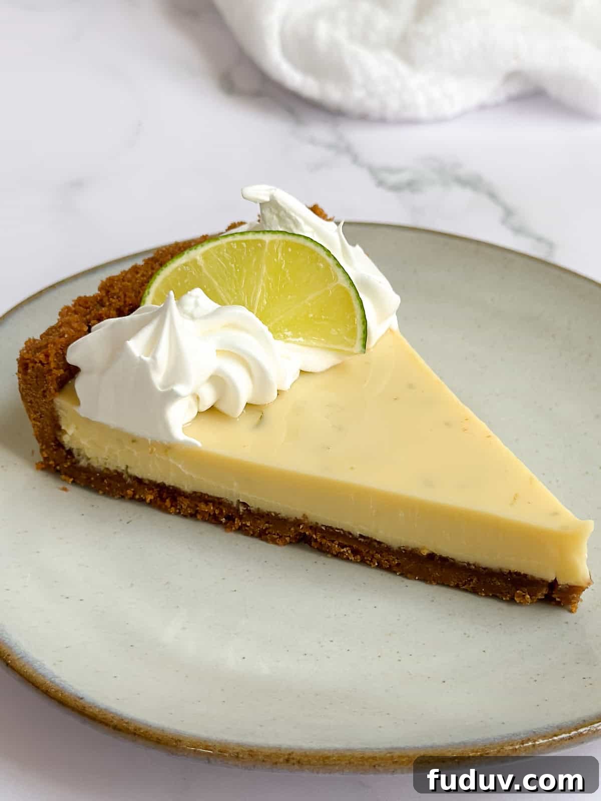 a single slice of key lime pie on a plate topped with whipped cream and a lime wedge.