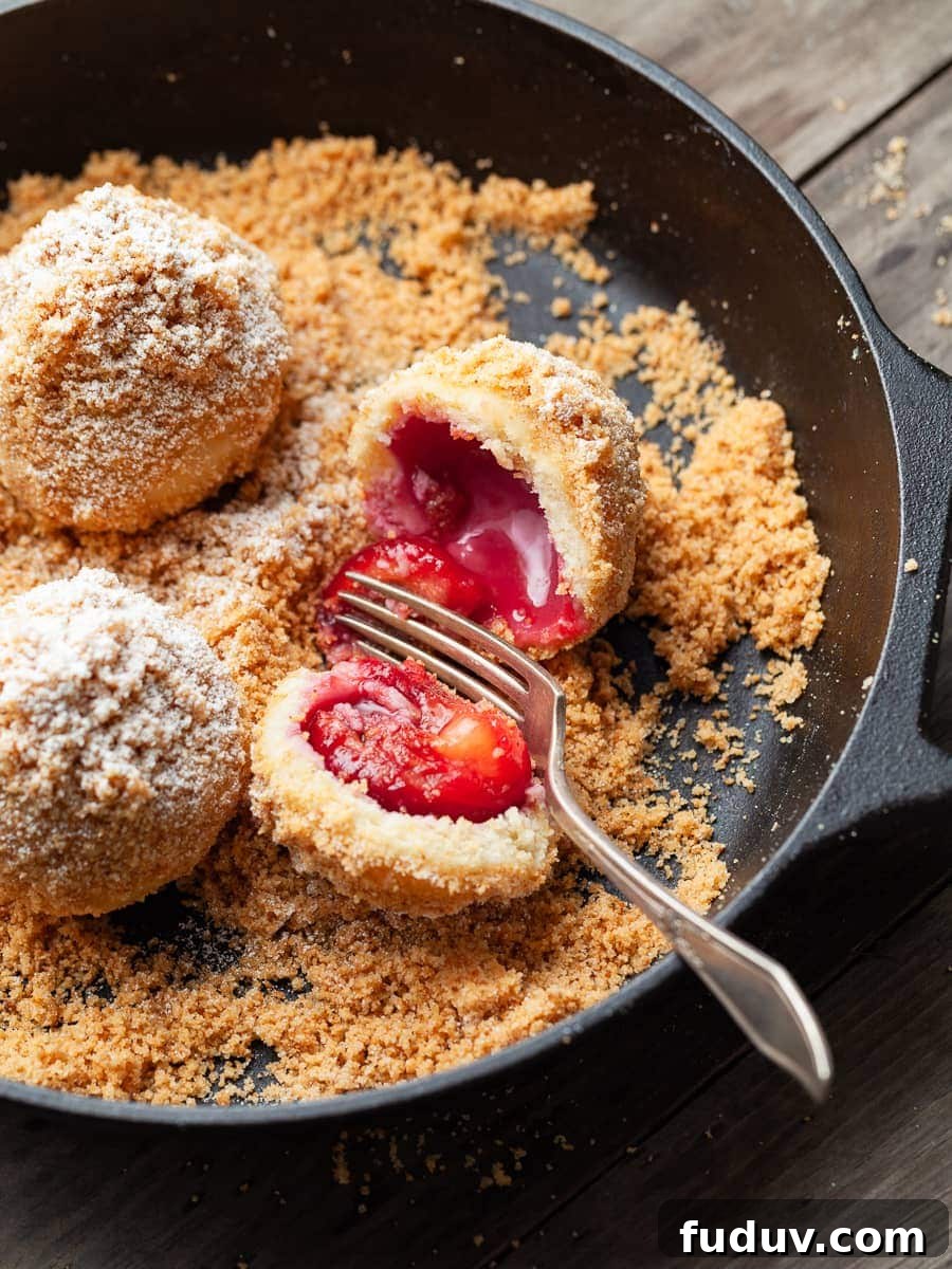 austrian plum dumplings in a cast iron skillet with two forks, one dumpling is cut in half to show the inside of the dumpling, Zwetschgenknödel