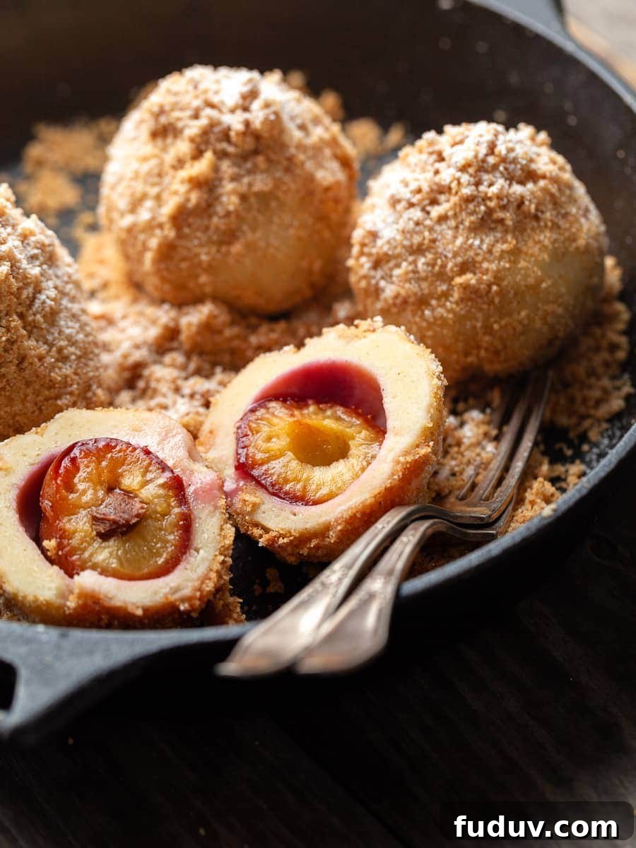 austrian plum dumplings in a cast iron skillet with two forks, one dumpling is cut in half to show the inside of the dumpling, Gluten Free Zwetschgenknödel