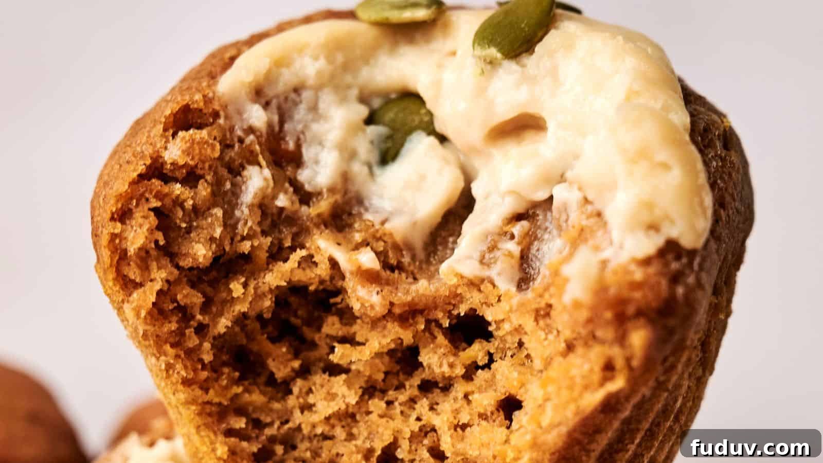 31 Cozy Cinnamon Recipes to Warm Your Home and Soul 12 Close-up of a muffin with a bite taken out, topped with cream and pumpkin seeds.