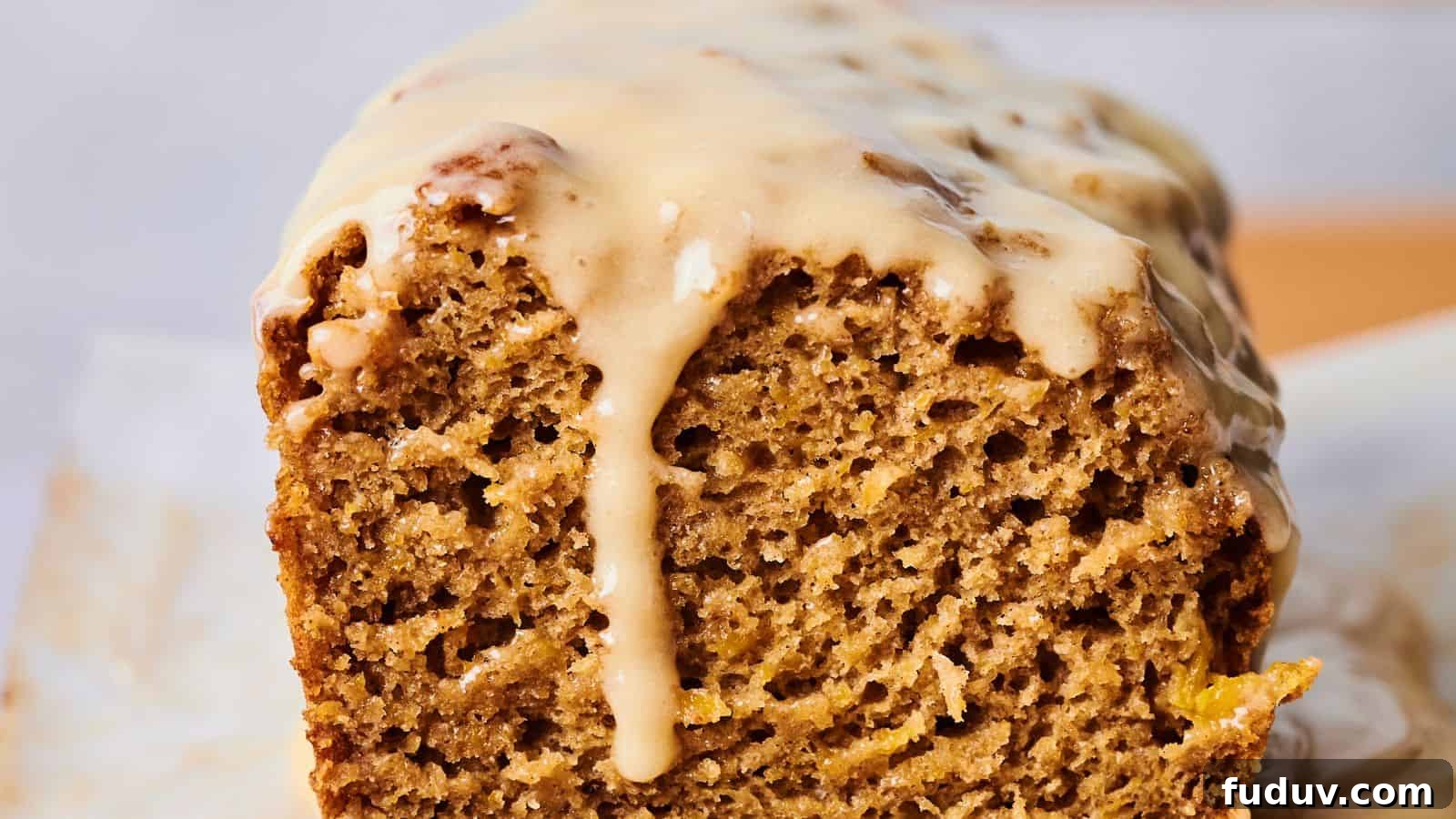 31 Cozy Cinnamon Recipes to Warm Your Home and Soul 15 A close-up of a sliced loaf of pumpkin bread with a light tan glaze dripped over the top. The bread has a moist and textured look, with visible air bubbles throughout.