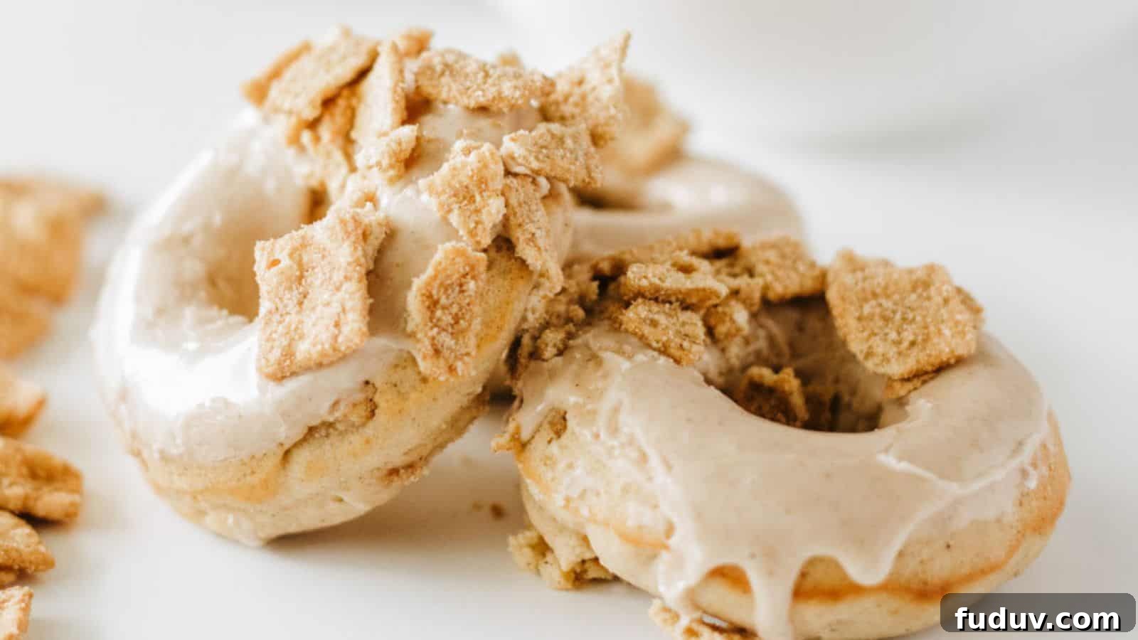 31 Cozy Cinnamon Recipes to Warm Your Home and Soul 27 Two glazed donuts topped with crumbled cereal pieces are placed on a white surface.